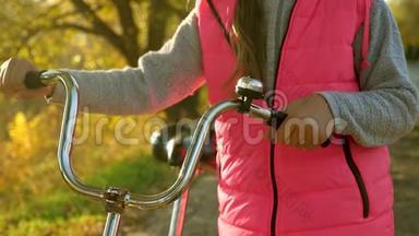 女孩的手拿着弯曲的自行车把手。 特写镜头。 女孩在秋天骑自行车在公园里散步。